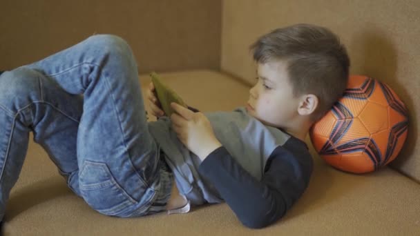 Boy playing games laying on the sofa.  - Filmati, video