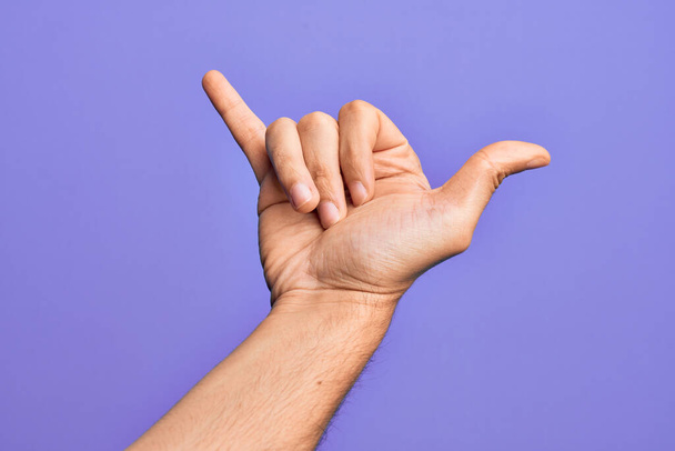 Hand of caucasian young man showing fingers over isolated purple background gesturing Hawaiian shaka greeting gesture, telephone and communication symbol - Photo, Image
