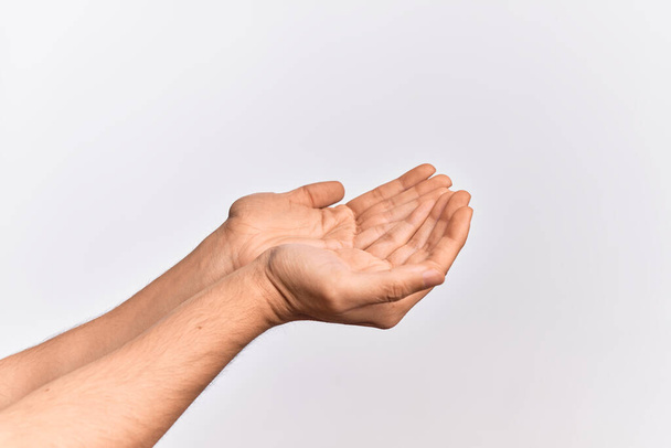 Hand eines kaukasischen jungen Mannes, der Finger über isoliertem weißem Hintergrund zeigt und mit beiden Händen Handschellen anlegt, offene Handflächen, die Hilfsgeste machen - Foto, Bild