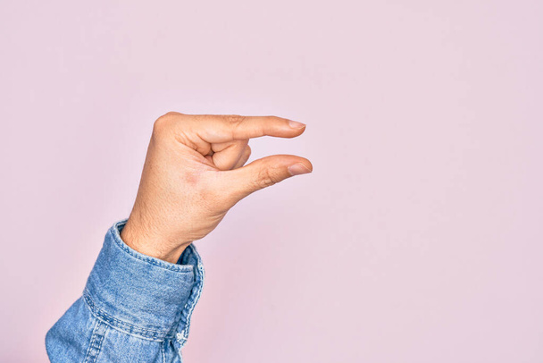 Hand van Kaukasische jongeman met vingers over geïsoleerde roze achtergrond plukken en nemen onzichtbare ding, houden object met vingers tonen ruimte - Foto, afbeelding
