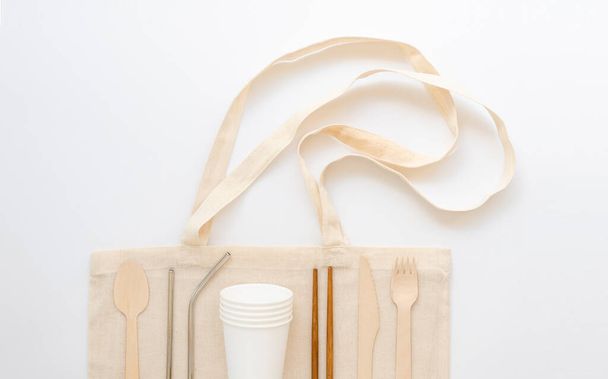 Набор экологически чистых многоразовых блюд и металлических чашек для питья на соломенной сумке. Концепция нулевых отходов на белом фоне
 - Фото, изображение