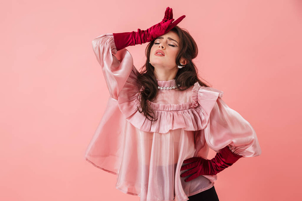 Portrait of a beautiful young brunette woman with bright makeup wearing fashionable clothes standing isolated over pink background, posing - Фото, зображення