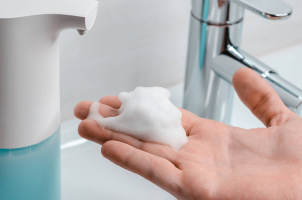 Automatic soap dispenser in the bathroom. Hand with soapy solution closeup - Foto, Imagem