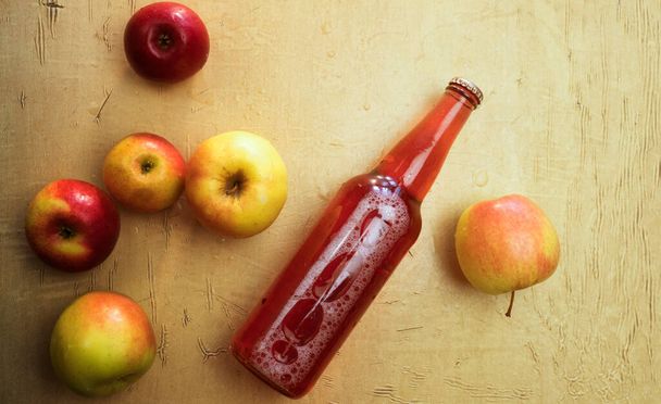 Achtergrond met een fles rode cider en verse appels die op tafel liggen. - Foto, afbeelding