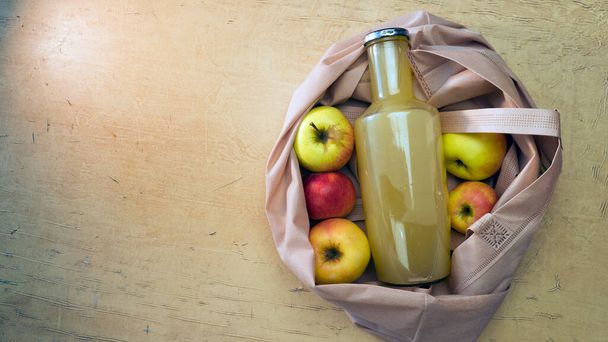 Egy üveg almalé fekszik egy ökotáskában, almával egy fából készült asztalon, fénymásoló hellyel.. - Fotó, kép