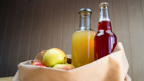 Elma suyu ve elma suyu şişeleri ahşap bir masanın üzerinde elmalarla bir eko torbasının içinde yatıyor.. - Fotoğraf, Görsel