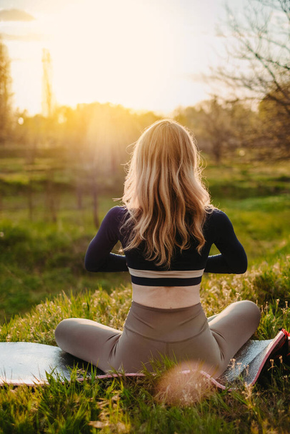 Schlankes Mädchen beim Yoga im Park bei Sonnenuntergang. Gesundheitsversorgung im Freien. Blick von hinten - Foto, Bild