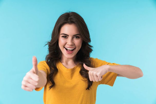 Image of a cheerful young pretty woman posing isolated over blue wall background showing thumbs up. - Foto, immagini