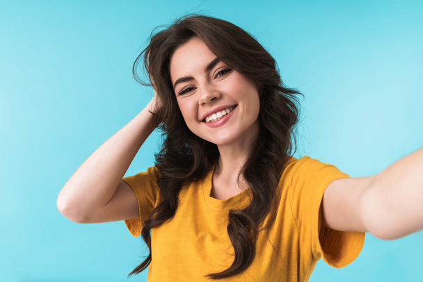 Image of emotional happy cheery young pretty woman posing isolated over blue wall background take a selfie by camera. - Foto, Imagem
