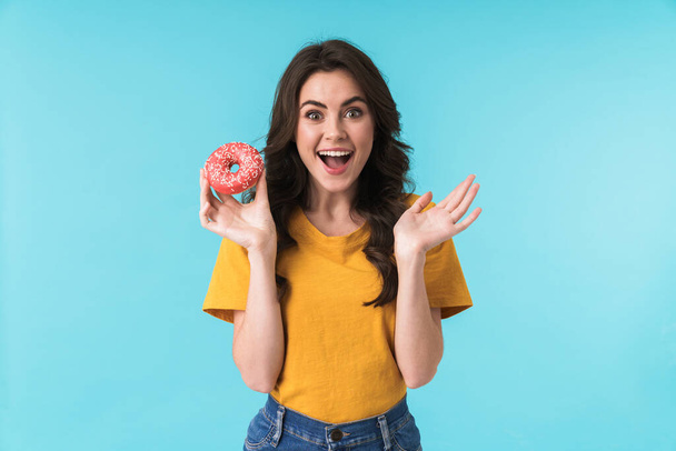 Image of pleased cheery young pretty woman posing isolated over blue wall background holding donut. - Foto, Imagem