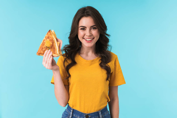 Image of happy optimistic young beautiful woman posing isolated over blue wall background holding sandwich. - Fotoğraf, Görsel