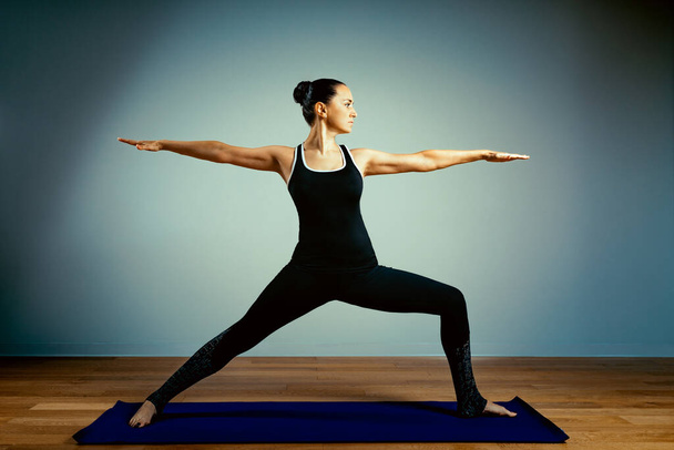 Atletische oudere vrouw doet yoga op een blauwe achtergrond - het concept van een gezonde levensstijl en een natuurlijk evenwicht tussen het lichaam en mentale ontwikkeling en veroudering. Actieve ouderdom. - Foto, afbeelding