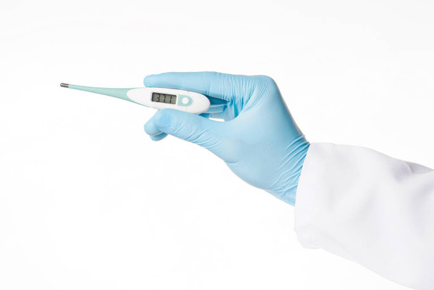 Close-up hand in rubber latex medicijn blauwe handschoen met een elektronische thermometer. Concept hitte, malaise, koorts, pijn. Geïsoleerd op witte achtergrond. - Foto, afbeelding
