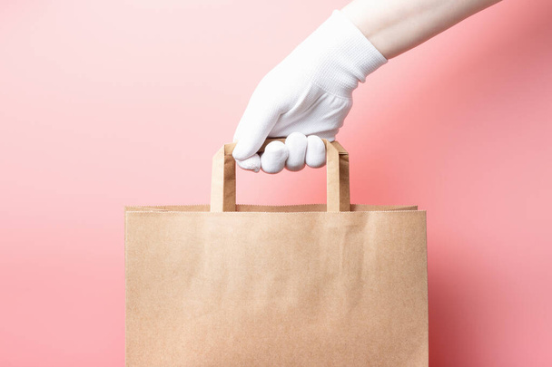 Női kéz egy fehér kesztyű tartja barna kartondoboz rózsaszín háttér, élelmiszer szállítási koncepció. - Fotó, kép