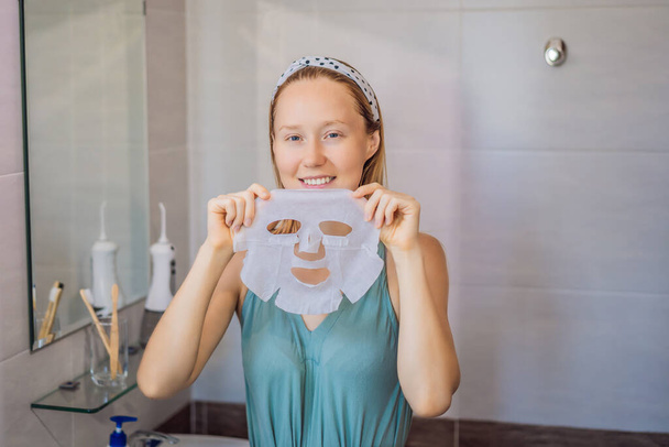 Young red-haired woman doing facial mask sheet. Beauty and Skin Care Concept - Φωτογραφία, εικόνα