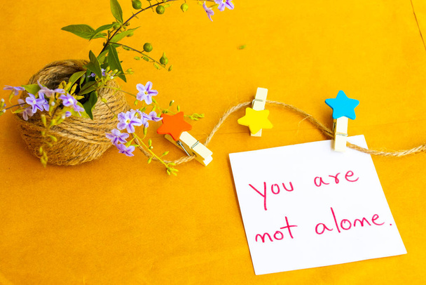 you are not alone message card handwriting with wooden star ,rope and purple flowers arrangement flat lay postcard style on background brown paper  - Фото, зображення