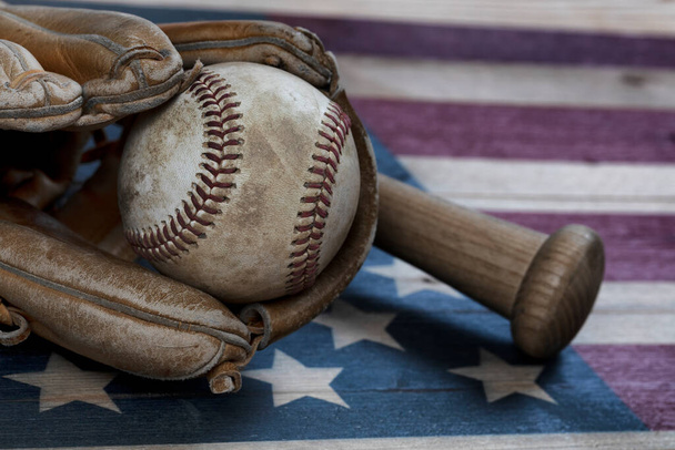 Вид крупным планом старого бейсбольного мяча, перчатки и традиционной деревянной летучей мыши на деревенском деревянном флаге США
 - Фото, изображение