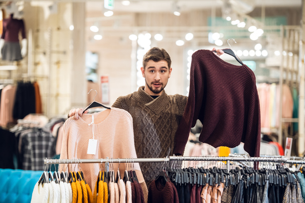 Un joven ayudando a su novia a encontrar el suéter adecuado en una tienda de ropa
 - Foto, imagen