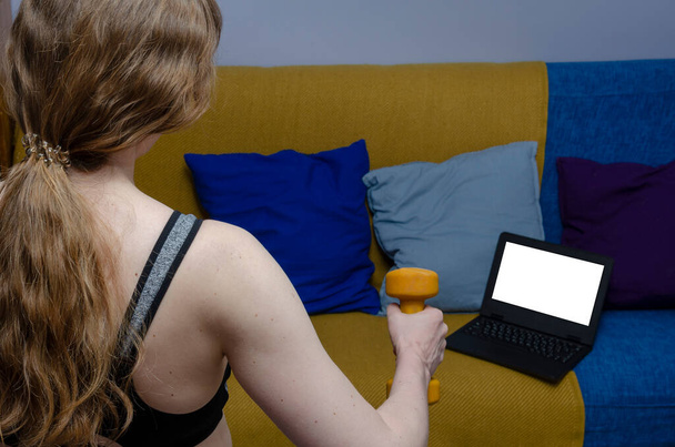 The girl is engaged in fitness at home. Looks at a trainer on a laptop. - Photo, Image
