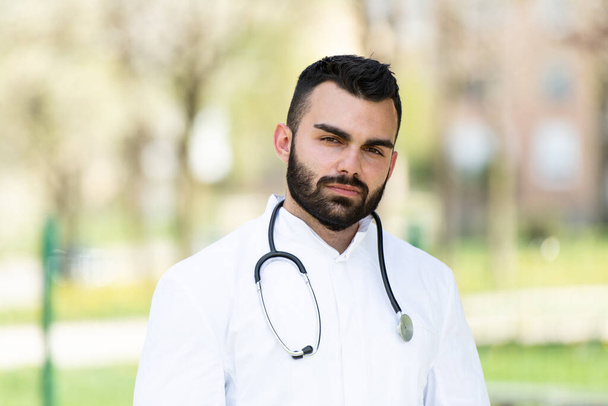 Portrait of a Tired Exhausted Male Caucasian Doctor With No Mask in Front of a Park - Coronavirus Covid-19 Virus Disease - Global Pandemic Outbreak - Photo, Image