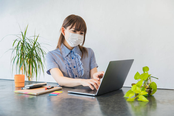 Woman wearing a mask and working remotely in the living room at home - Photo, Image