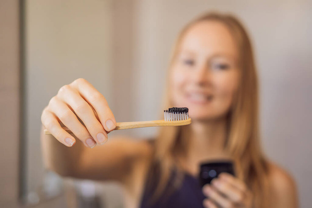 young woman brushing her teeth with a black tooth paste with active charcoal, and black tooth brush in her bathroom - Foto, afbeelding