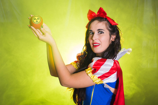 Eine als Märchenfigur verkleidete Frau hält ein Warnsymbol für radioaktive atomare ionisierende Strahlung auf einem Apfel. Kern- und Strahlenmesskonzept. - Foto, Bild