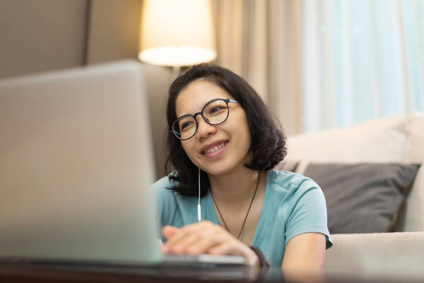 Beautiful Asian girl in blue shirt and eyeglasses enjoying online class with internet wireless technology. Happy smiling Young woman using laptop computer during quarantine and isolated. Work from home. Covid 19, Coronavirus - Foto, afbeelding