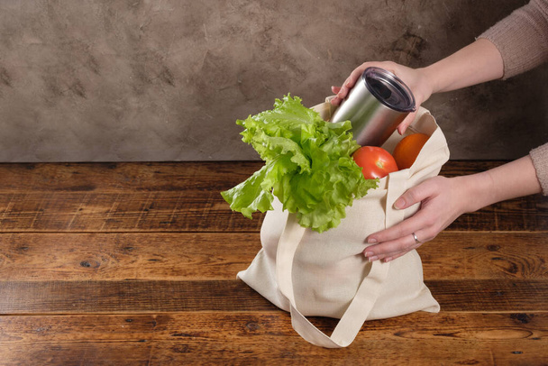 Eco-friendly groceries bag. Reusable shopping bag with fresh fruits and greens on wooden background. Bag , green salat, orange , tomatos on brown table. Healthy food, useful organic products. Copy space. - Foto, imagen