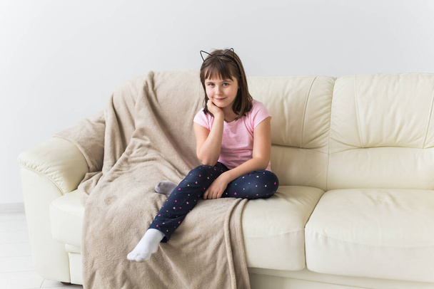 Słodka dziewczyna z kocimi uszami siedząca na kanapie. Dzieci i koncepcja dzieciństwa. - Zdjęcie, obraz