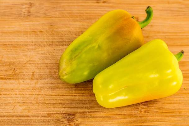 pair of yellow green sweet peppers pods lie on a brown wooden background - Photo, Image