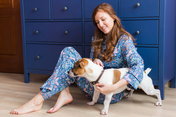 Ευτυχισμένη νεαρή γυναίκα που κάθεται με το σκύλο της στο σπίτι. Ιδιοκτήτης κατοικίδιων ζώων, ζώα και φιλία. - Φωτογραφία, εικόνα