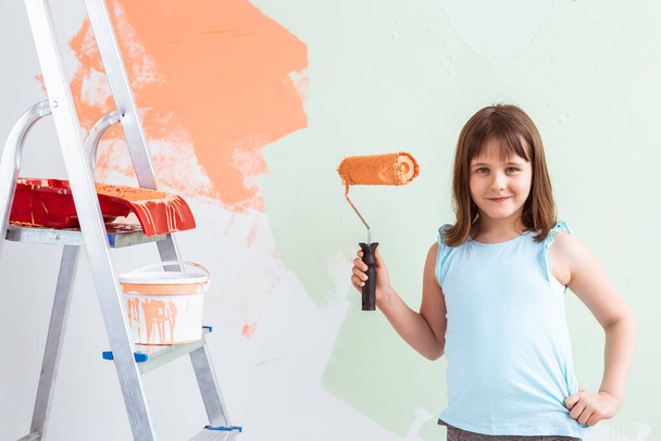 Reparación en el apartamento. La niña feliz pinta la pared con pintura naranja. Concepto de renovación y redecoración
. - Foto, imagen