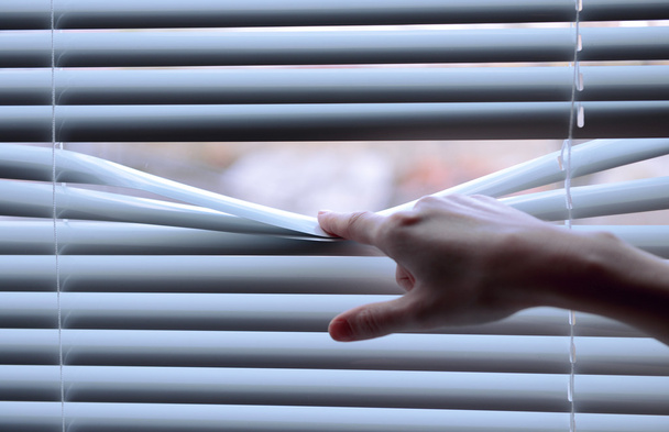 Female hand separating slats of venetian blinds with a finger to see through - Foto, imagen