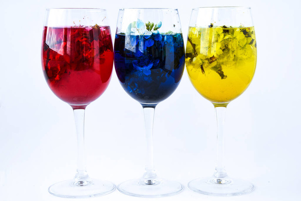 three wine glasses of spring blossom flowers, with yellow, red and blue water on white background, bar and spring time cocktails, spa alcohol - Fotografie, Obrázek