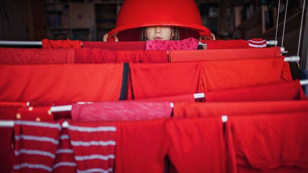 Linda niña ayudando a colgar la ropa roja después del lavado, mantener como colores juntos para evitar que el color se desvanezca, consejos de tareas, estilo de vida interior
 - Foto, Imagen