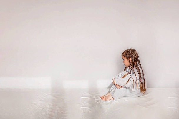 Tiny cute girl sitting in the white empty space with sad feelings, negative emotions concept, studio shot - Фото, изображение
