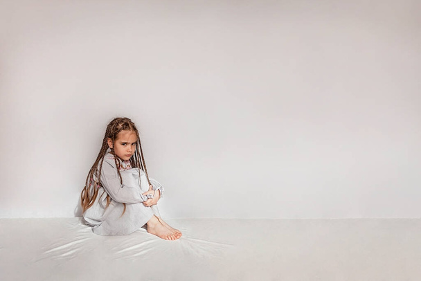 Μικρό χαριτωμένο κορίτσι κάθεται στο λευκό κενό χώρο με λυπημένα συναισθήματα, αρνητική έννοια συναισθήματα, στούντιο πυροβόλησε - Φωτογραφία, εικόνα