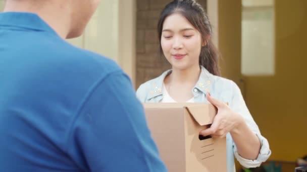郵便配達の若い男は、顧客、アジアの女性に送信するための小包ボックスを保持し、屋外で配達された小包を受け取るために携帯電話のQRコードを介して署名し、支払う. - 映像、動画