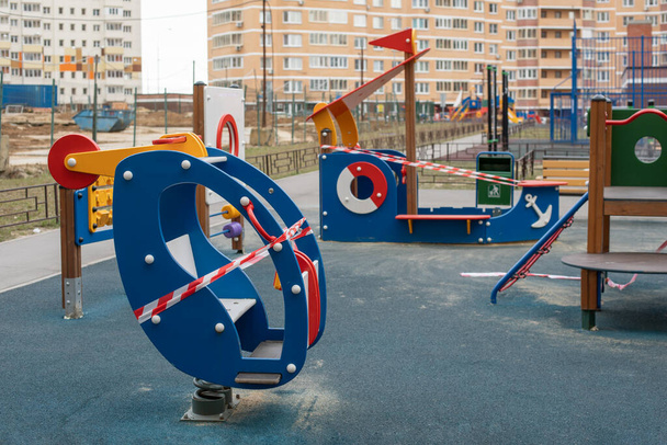 Ein leerer Spielplatz, in ein gestreiftes Klebeband gehüllt, bleibt zu Hause. Sanitäre Behandlung einer Hubschrauberschaukel für Kinder, um die Epidemie des Coronavirus covid-19 zu verhindern - Foto, Bild