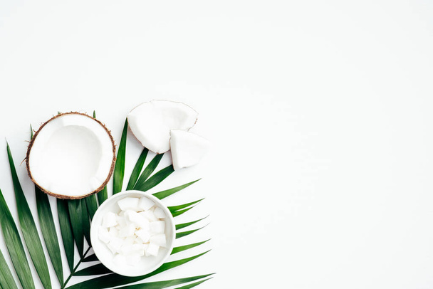 Coconut fruit with half and grated coconut in bowl, tropical palm leaf on white background. Flat lay, top view. Summer background. - 写真・画像
