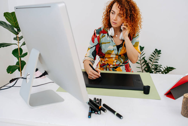 Focused artist woman talking on the phone while painting behind work desk - Foto, Bild