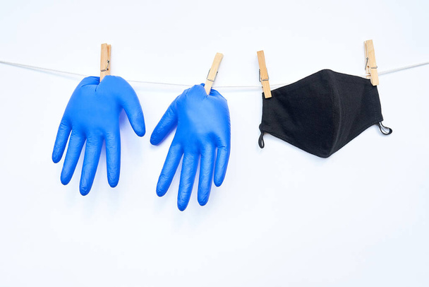 Blue medical gloves and black reusable fabric mask hang on cord, attached with pins. - Foto, Imagem
