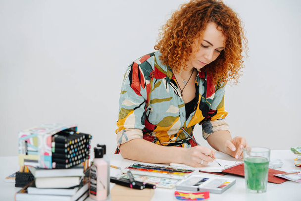Artista enfocado pintando con un pincel en un escritorio desordenado y desordenado
 - Foto, imagen
