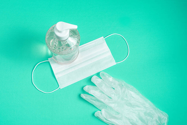 Container with alcohol gel, gloves and surgical mask on the light blue background - Фото, зображення