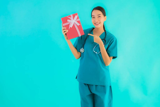 Portrait beautiful young asian doctor woman show red gift box on blue isolated background - Photo, Image
