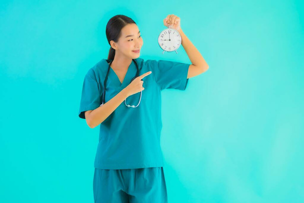 Портріат, вродлива азіатська жінка, показує годинник або сигналізацію на синьому ізольованому фоні. - Фото, зображення