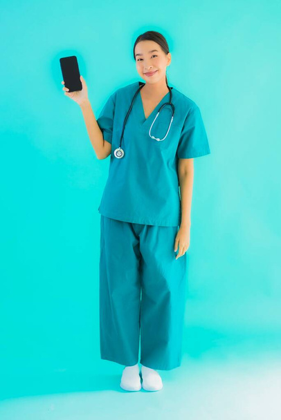 Портрет красива молода азіатська лікарка показує смартфон на синьому ізольованому фоні
 - Фото, зображення