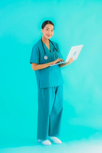 Портрет красива молода азіатська лікарка з ноутбуком або комп'ютером на синьому ізольованому фоні
 - Фото, зображення