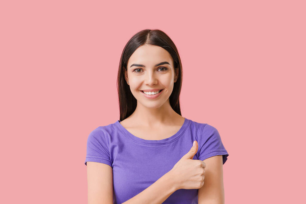 Beautiful young woman with healthy teeth showing thumb-up gesture on color background - Photo, image